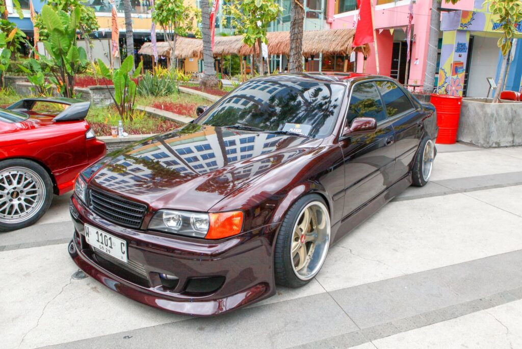 A sleek maroon sedan parked on an urban street with tropical plants nearby, showcasing modern car design.