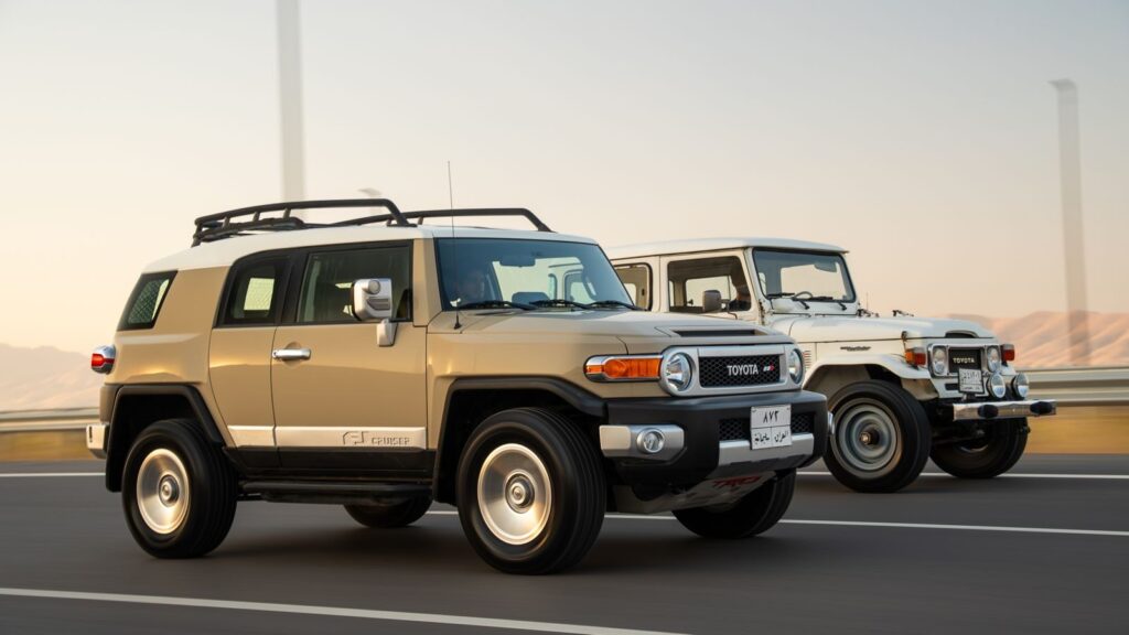 Dynamic shot of a Toyota FJ Cruiser and classic Land Cruiser driving on a desert highway.