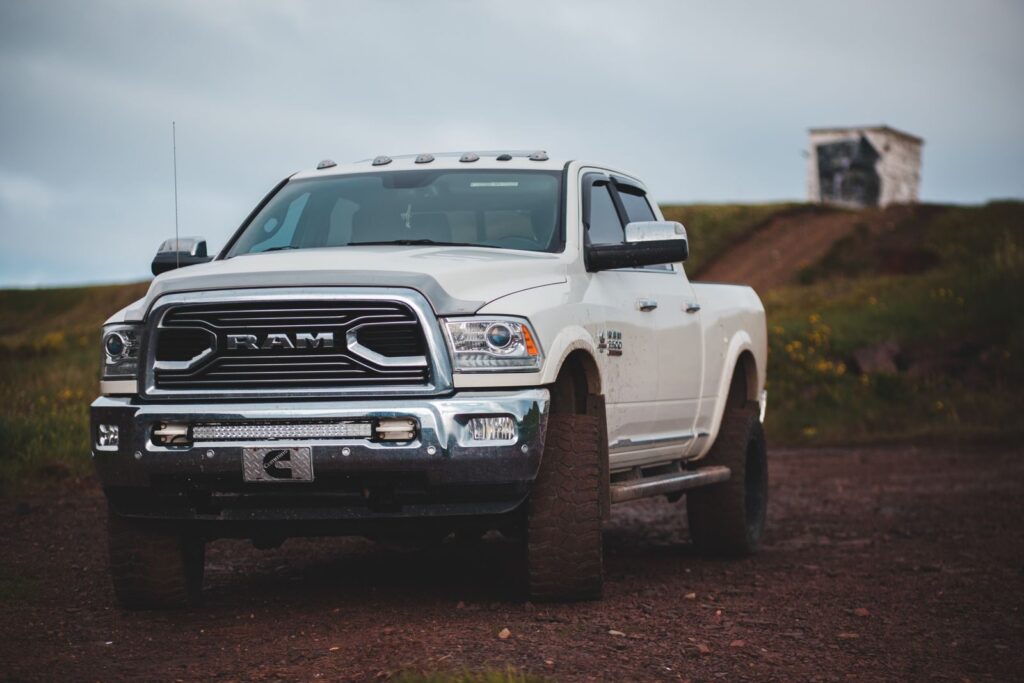 Front part of modern white pickup parked on road covered with pebbles under grey sky