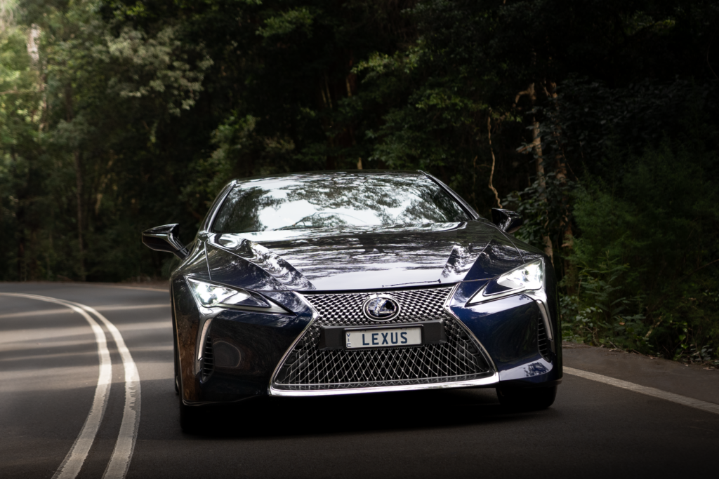 A luxury Lexus car driving through a forest road in Sydney, Australia, captured during the day.