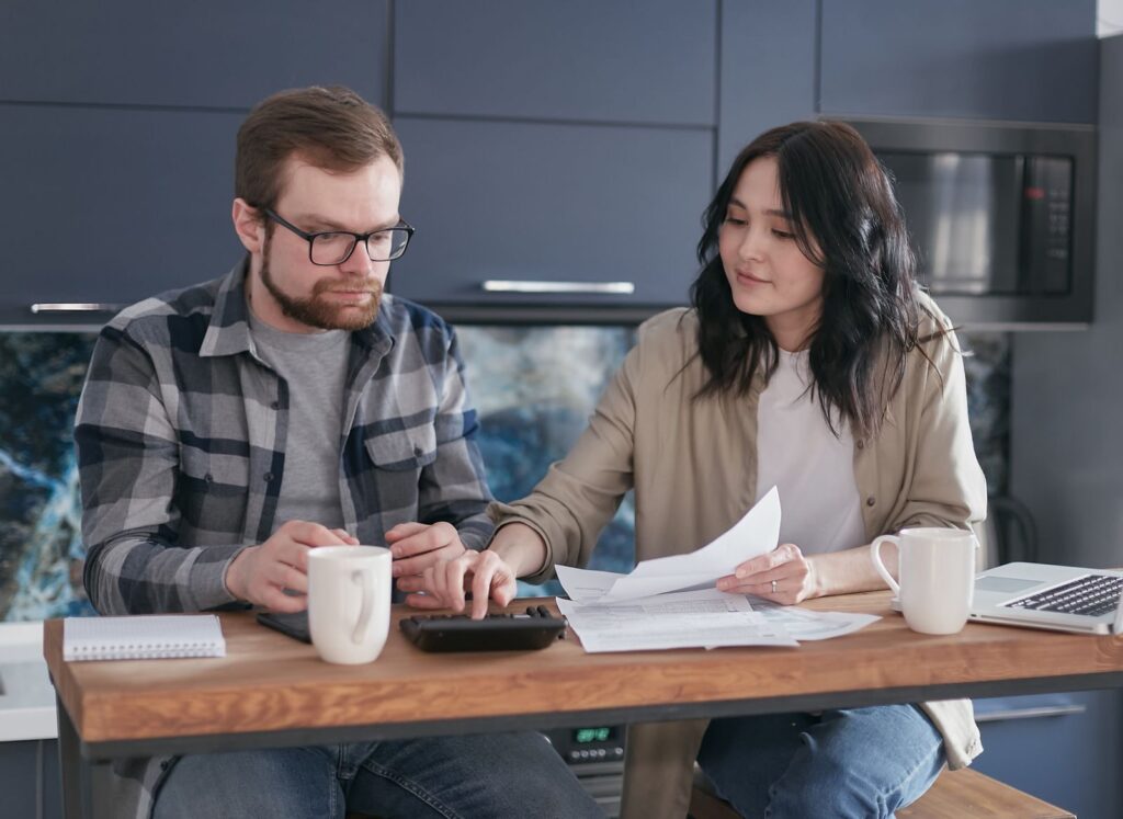 Couple sitting at home managing finances with documents and calculator.
