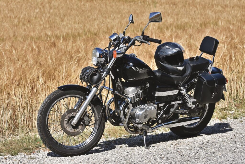 Classic black motorcycle with helmet parked on gravel road against golden field.