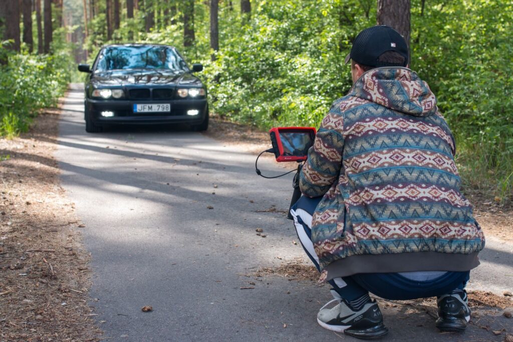 Photographer films car driving along forest road using specialized equipment.