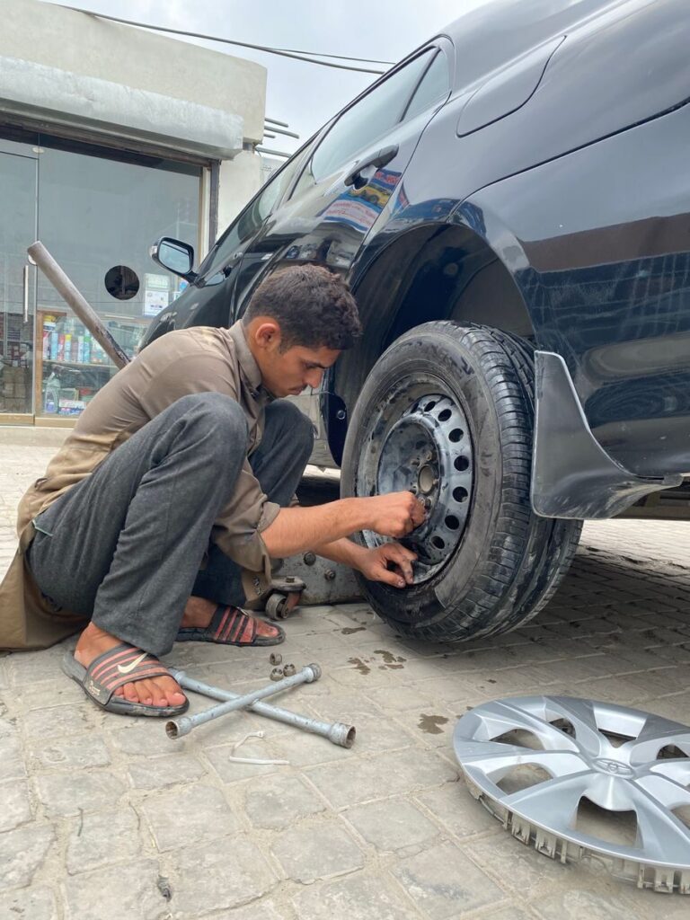 Mechanic crouched fixing a tire outdoors, showcasing vehicle maintenance.