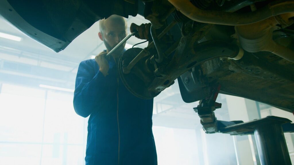 Mechanic in blue coverall fixing a vehicle in a well-lit auto workshop.
