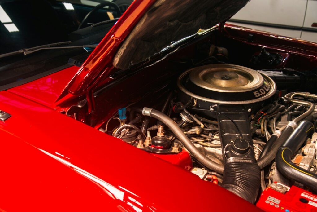 A red car engine with the hood open in a garage