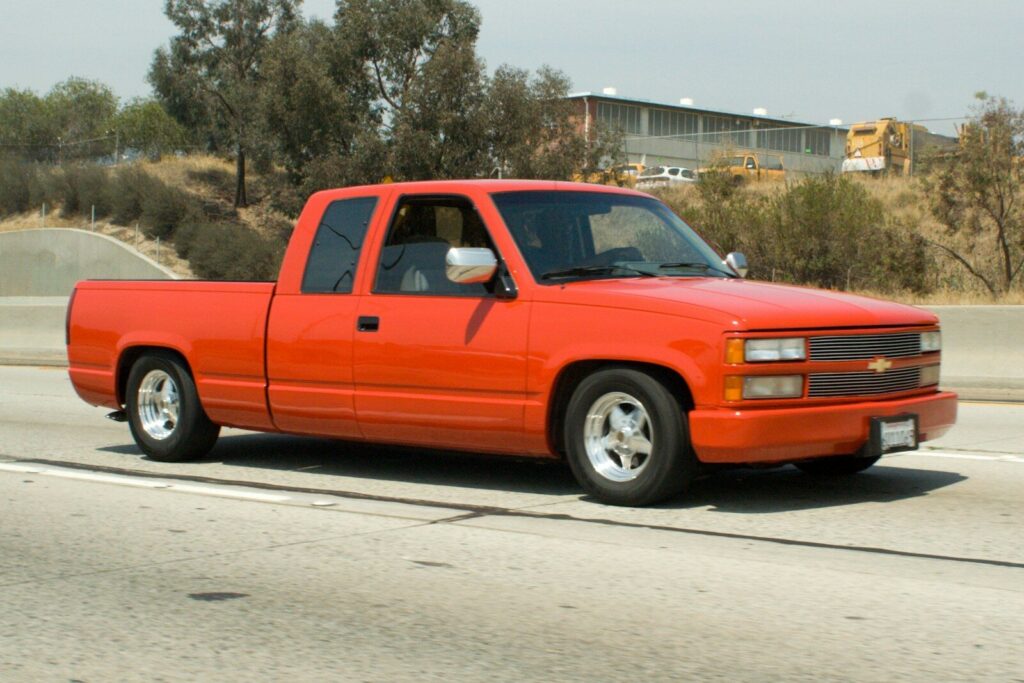A bright orange pickup truck driving on a highway