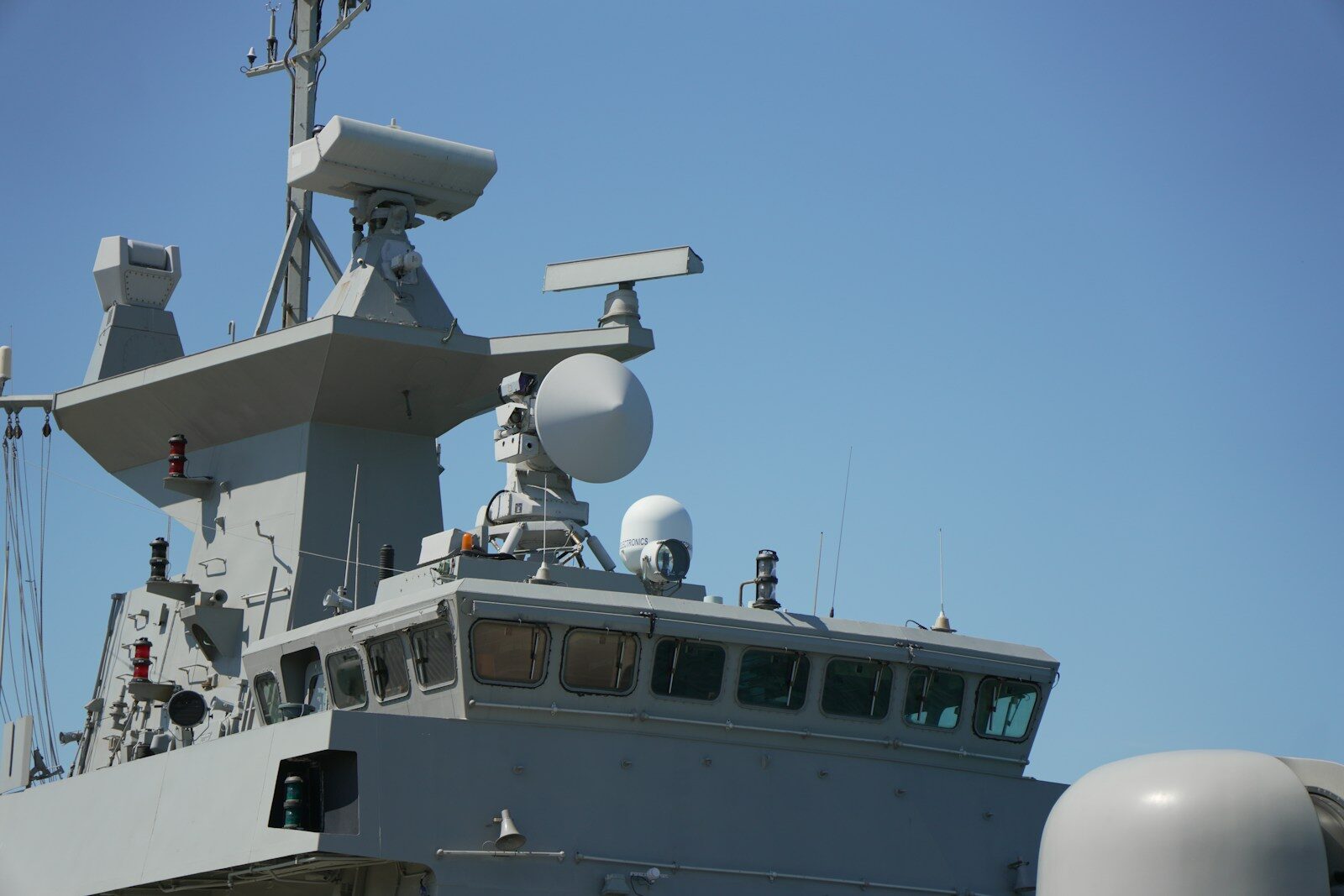 Naval ship's bridge and radar systems against a blue sky