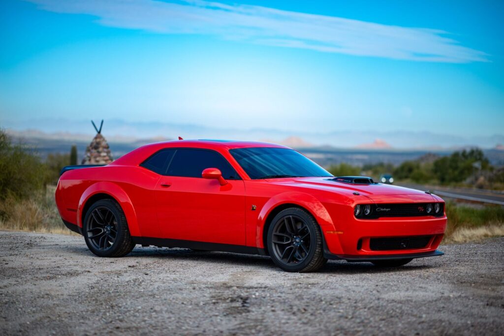 Red Dodge Challenger muscle car parked in a scenic Arizona landscape with clear blue skies.