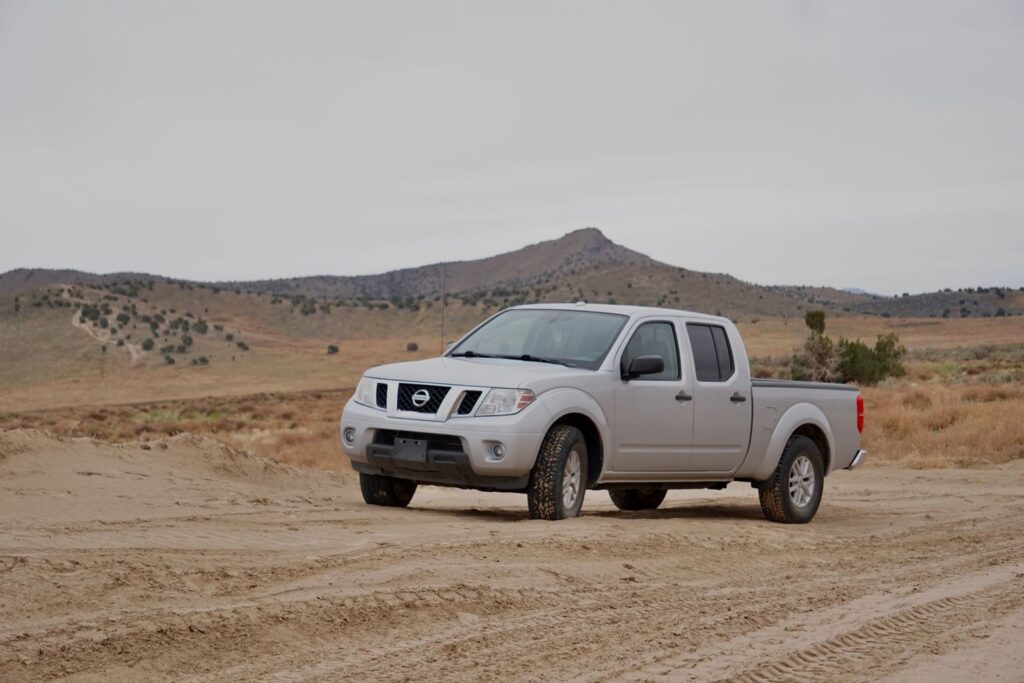 Silver pick-up truck parked on a rural dirt road in a rugged countryside landscape.